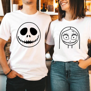 May include: A couple wearing white t-shirts with black and white cartoon faces printed on them. The man's shirt features Jack Skellington's face, while the woman's shirt features Sally's face.