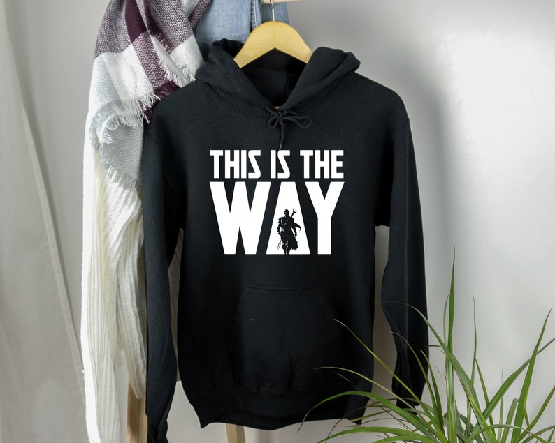 May include: Black hooded sweatshirt with white text that reads "This is the Way" and a silhouette of a figure in a Mandalorian helmet and armour.