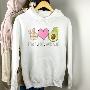 Könnte beinhalten: Weißer Hoodie mit einem Peace-Zeichen, einem Herzen und einer Avocado-Grafik. Der Text "Peace. Love. Avocados" ist unter der Grafik gedruckt.