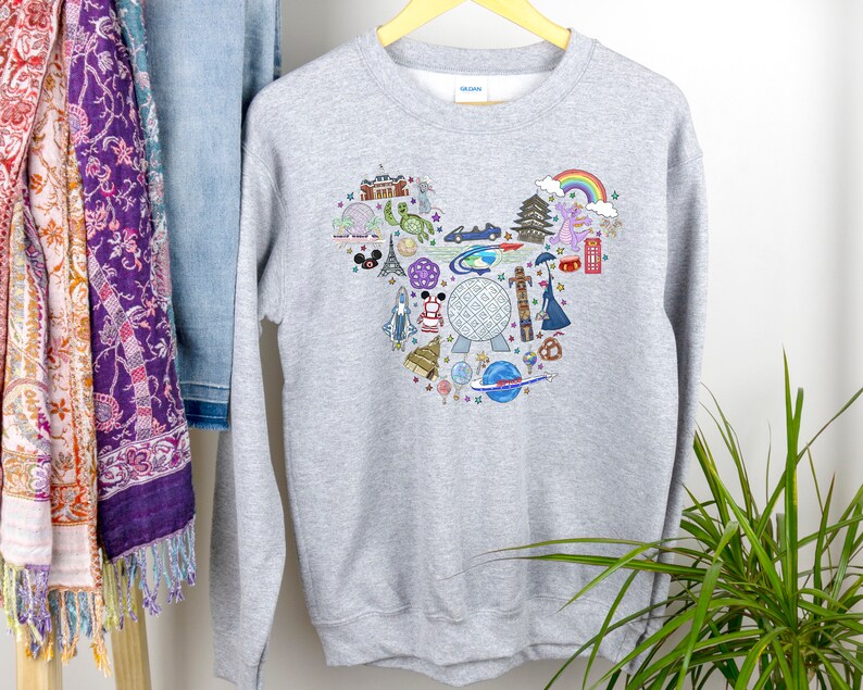 May include: Grey sweatshirt with a Mickey Mouse-shaped design featuring various Disney park icons, including the Spaceship Earth, Cinderella's Castle, and the Haunted Mansion.