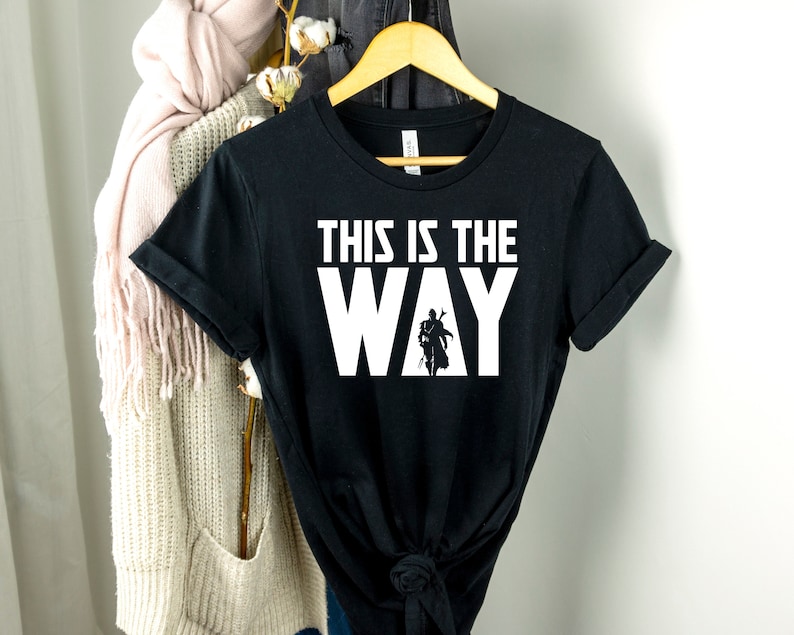 Op de afbeelding: Zwart T-shirt met witte tekst "This is the Way" en een silhouet van een Mandalorian-personage.