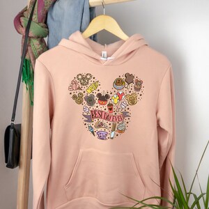 May include: A light pink hoodie with a Mickey Mouse head design featuring various Disney icons and the text "BEST DAY EVER".