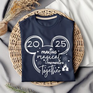 以下が含まれることがあります： 白いミッキーマウスの頭のデザインが施されたネイビーブルーのTシャツ。ミッキーマウスの頭には、耳に20と25の数字があります。ミッキーマウスの頭の中には、「Making magical memories together」という文字があります。