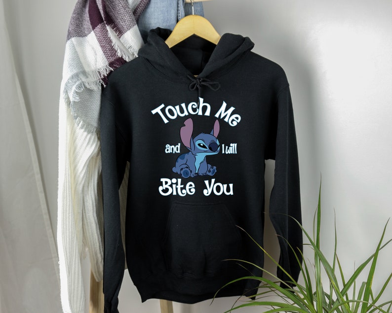 Puede incluir: Sudadera con capucha negra con un personaje azul Stitch de Lilo & Stitch. El texto en la sudadera dice "Touch Me and I Will Bite You".