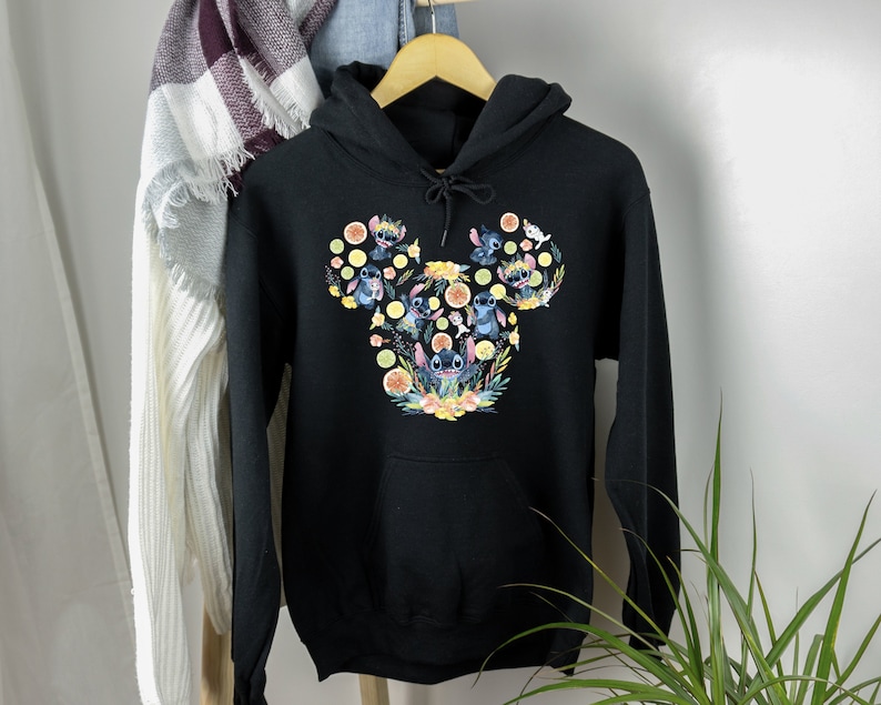 K&ouml;nnte beinhalten: Schwarzer Kapuzenpullover mit einem bunten Motiv von Stitch-Charakteren in Form eines Mickey-Maus-Kopfes. Das Motiv zeigt Stitch-Charaktere mit Blumen und Zitronen.