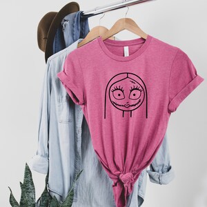 May include: A pink t-shirt with a black line drawing of Sally from the Nightmare Before Christmas.