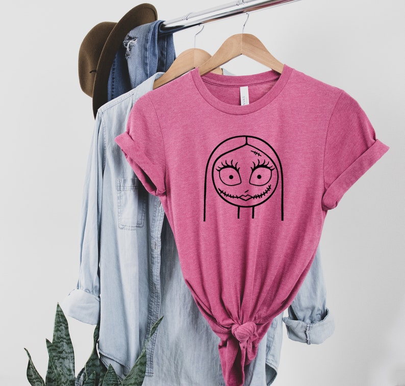 May include: A pink t-shirt with a black line drawing of Sally from the Nightmare Before Christmas.