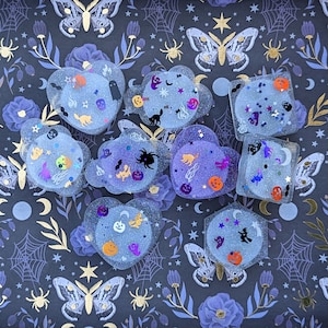 May include: A set of ten Halloween-themed resin ornaments featuring various spooky and cute designs, including ghosts, bats, pumpkins, and spiders. The ornaments are translucent and have a glittery finish.
