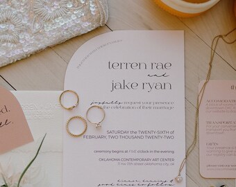May include: Wedding invitation with the names Terren Rae and Jake Ryan, featuring gold rings, a beaded clutch, a white flower, and a pair of sneakers. The invitation includes the date, time, and location of the ceremony.
