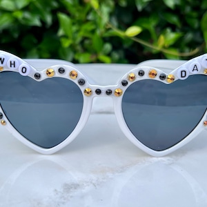 May include: White heart-shaped sunglasses with black and gold rhinestones and the words "WHO DAT" on the frames.
