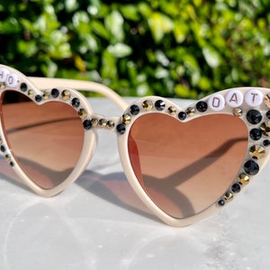 May include: White heart-shaped sunglasses with black and gold rhinestones and the words "WHO DAT" on the frames.