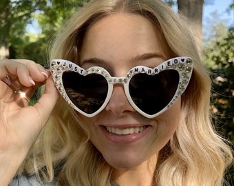 May include: White heart-shaped sunglasses with rhinestones and the words "JUST MARRIED" on the lenses.