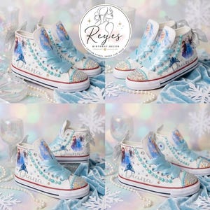 May include: White high-top sneakers featuring light blue satin ribbon laces, pearl accents, and a graphic print of animated characters. The shoes are personalized with the name Diana in script, silver bows at the heels, and crystal-embellished toes.