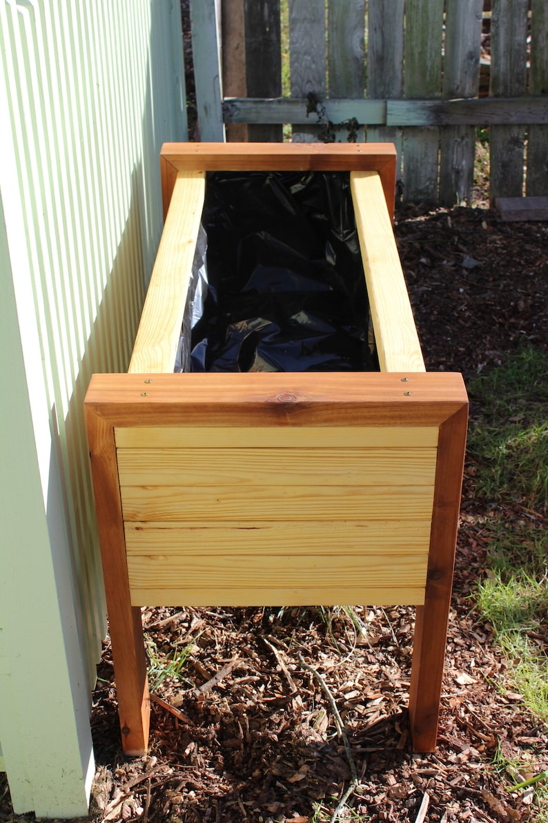 wood raised garden bed plans include how to line your planter with black plastic as shown in this image. It allows water to drain properly, without damaging the surrounding wood and compromising the strength of your newly built planter