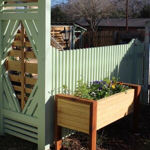a modern planter sits outside against an arbor, filled with green plants and flowers it shows it can eliminate the need to bend over and ache your back when weeding and planting