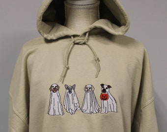 May include: A beige hooded sweatshirt featuring an embroidered design of four dogs wearing white ghost costumes. One dog is holding an orange jack-o'-lantern pumpkin in its mouth. The hoodie includes a matching drawstring at the neckline.