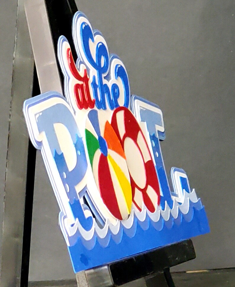Pode incluir: Uma placa 3D azul e branca que diz "Go to the Pool" com uma bola de praia colorida e um salva-vidas vermelho e branco.