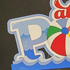 Pode incluir: Uma letra "P" azul e branca com uma bola de praia e ondas. A letra faz parte de uma palavra maior, possivelmente "Piscina" ou "Festa".