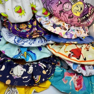 Peut inclure: Une pile de chouchous en tissu colorés avec différents personnages de dessins animés imprimés dessus. Les chouchous sont faits d'un tissu doux et extensible et sont parfaits pour retenir les cheveux.