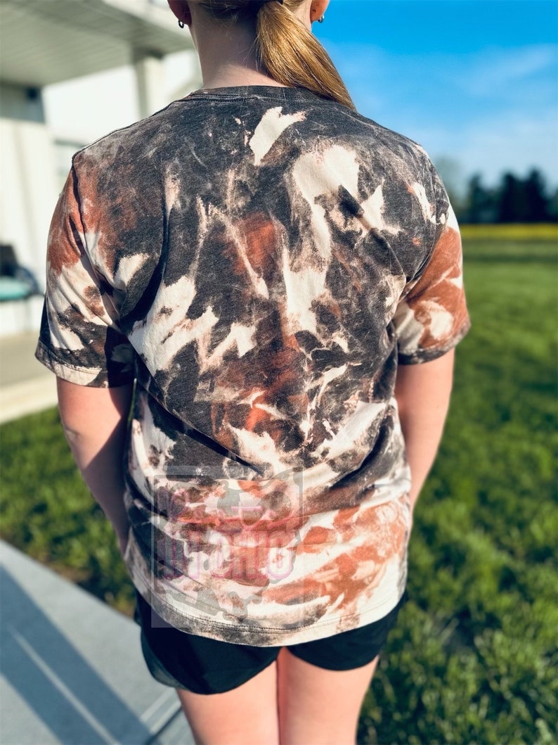 Może przedstawiać: Koszulka tie-dye w kolorze brązowym, czarnym i białym z kr&oacute;tkim rękawem i okrągłym dekoltem.