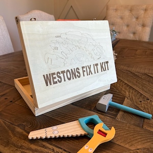 May include: A wooden toy tool set in a box with the words "Westons Fix It Kit" engraved on the lid. The set includes a saw, wrench, hammer, and screwdriver. The tools are painted with bright colors and have cartoon faces.