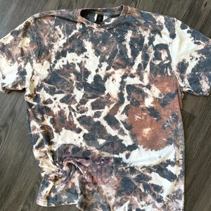 Może przedstawiać: Biała koszulka z brązowym i czarnym wzorem tie-dye.