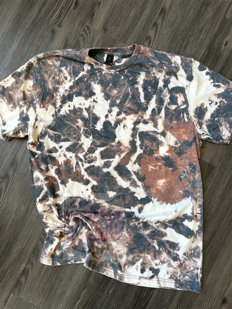 Może przedstawiać: Biała koszulka z brązowym i czarnym wzorem tie-dye.