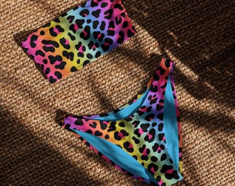 May include: A two-piece swimsuit set featuring a vibrant rainbow leopard print. The set includes a bandeau top and high-waisted bottoms with a turquoise blue lining. The colorful pattern includes pink, orange, yellow, green, and purple spots on a black background.
