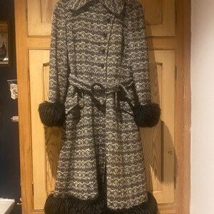 May include: A long black and white patterned coat with a black belt and black fur trim around the cuffs and hem.