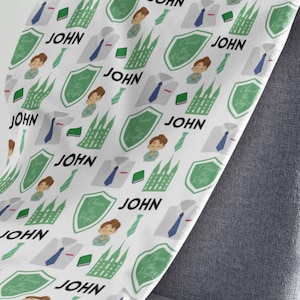 May include: White fleece blanket with a repeating pattern of a green temple, a boy with brown hair praying, a white shirt with a blue tie, a green tie, a green book, and the word "JOHN".