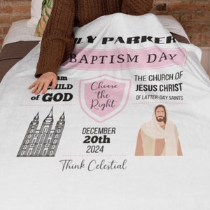 May include: A white fleece blanket with a pink and black design. The blanket features a temple, a shield with the text "Choose the Right", and a figure of Jesus Christ. The text "I am a Child of God" and "The Church of Jesus Christ of Latter-day Saints" are also included. The date "December 20th 2024" and the phrase "Think Celestial" are printed on the blanket.