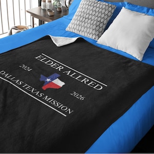 May include: Black fleece blanket with white text that reads "Elder Allred 2024-2026 Dallas Texas Mission" and a small image of the Texas flag.