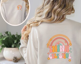 Puede incluir: Una sudadera de color arena con un arcoíris y el texto "Think Celestial" en una fuente retro. La sudadera tiene mangas largas y cuello redondo.