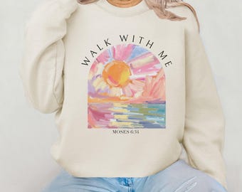 May include: Cream-colored sweatshirt with a colorful graphic of a sun over water, with the text "WALK WITH ME" and "MOSES 6:34". The design features shades of pink, yellow, and blue.