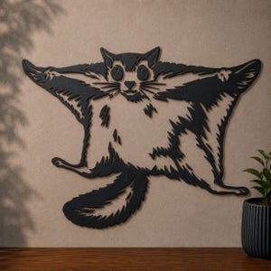 May include: A black metal wall art piece shaped like a flying squirrel with its limbs extended in a gliding pose. The design features cut-out details for the eyes, nose, and fur texture, creating a silhouette of the animal with a long tail.
