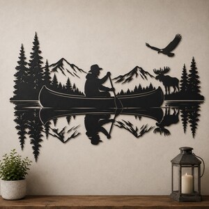 May include: A black metal wall art piece depicting a silhouette of a person paddling a canoe on a lake, surrounded by pine trees, mountains, a moose, and a flying eagle. The design includes a mirrored reflection effect of the scene below.