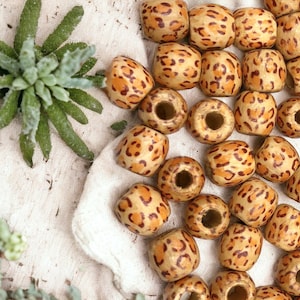 May include: A collection of wooden beads with a leopard print pattern. The beads are brown and orange with black spots.