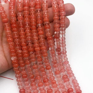 May include: A strand of pink and clear round gemstone beads. The beads are translucent and have a slight shimmer. The beads are strung on a clear thread.