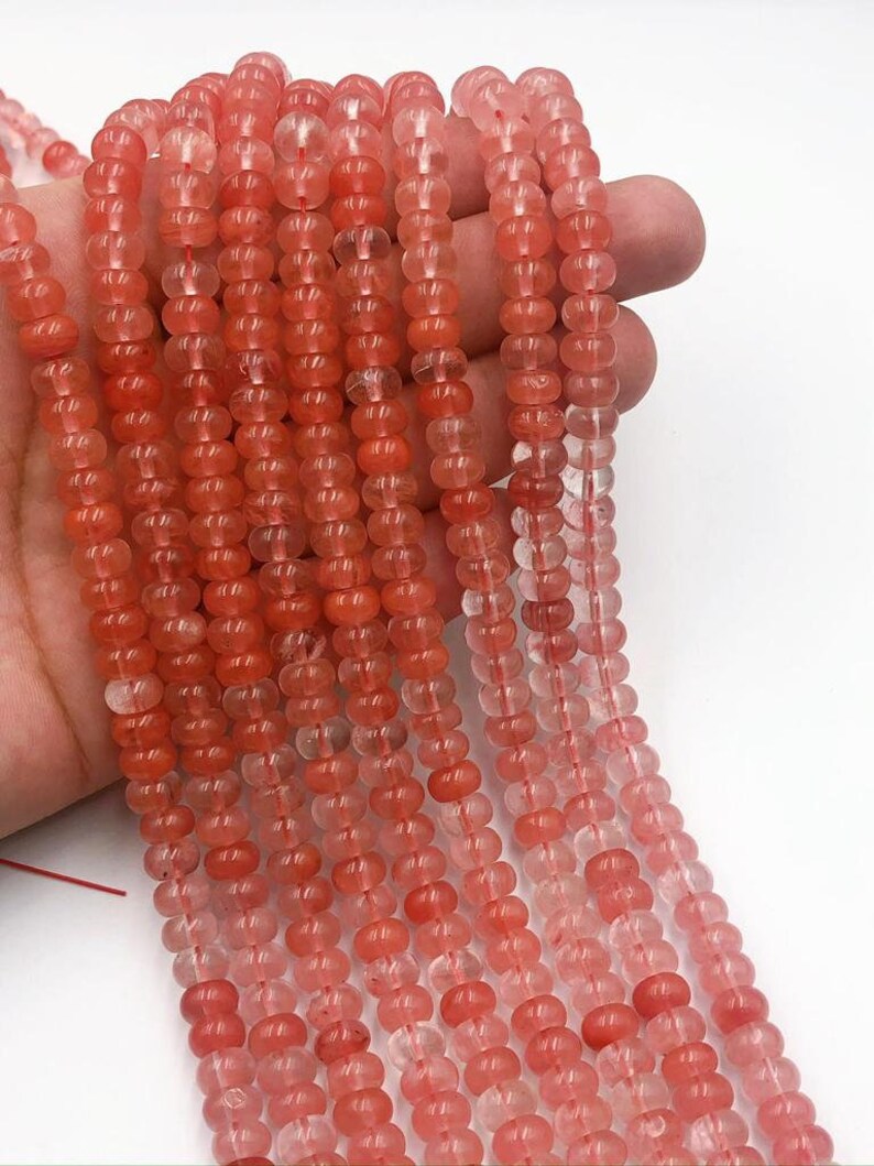 May include: A strand of pink and clear round gemstone beads. The beads are translucent and have a slight shimmer. The beads are strung on a clear thread.