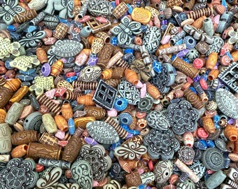May include: A collection of assorted beads in various shapes and colors. The beads include butterflies, flowers, and geometric designs in shades of brown, beige, blue, and orange. Some beads have intricate patterns and textures.
