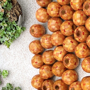 May include: A collection of wooden beads with a geometric pattern in shades of orange and brown. The beads have a hole in the center for stringing.
