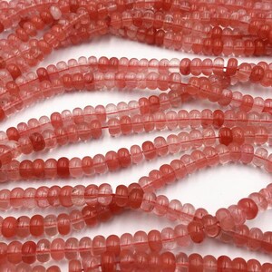 May include: A strand of translucent pink and red gemstone beads. The beads are round and have a slightly faceted appearance.
