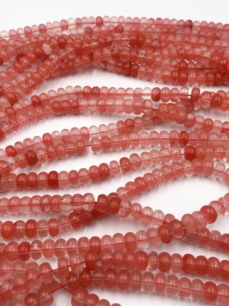 May include: A strand of translucent pink and red gemstone beads. The beads are round and have a slightly faceted appearance.