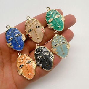 May include: Six gold-tone metal charms shaped like faces with different colored enamel. The faces have closed eyes and a stylized design.