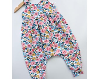 May include: A white jumpsuit with a floral print in shades of pink, blue, yellow, and green. The jumpsuit has a sleeveless bodice and a gathered waist. The legs are wide-legged and have a cuffed hem.