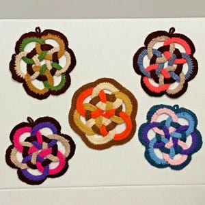 Pode incluir: Cinco pegadores de panela de crochê em várias cores e padrões. Os pegadores de panela são circulares e apresentam um design de nó. As cores incluem marrom, verde, laranja, azul e rosa.