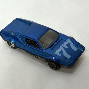 May include: A blue die-cast toy car with the number "77" printed on the bonnet. The toy car has black wheels and a silver undercarriage. The car is a vintage model.