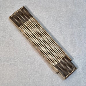 May include: A vintage wooden folding ruler with brown painted edges. The ruler is closed and has a worn, aged appearance.