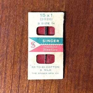 以下が含まれることがあります： ヴィンテージのシンガーミシン針のパッケージ。 パッケージは長方形で、赤と緑のアクセントがあります。 パッケージのテキストには、「SINGER machine Needles」、針のサイズ、および「60 to 80 cotton a silk」が含まれています。