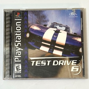 Op de afbeelding: PlayStation-gamecase voor "Test Drive 6". De cover toont een blauwe sportwagen met witte strepen tegen een rokerige achtergrond. Het PlayStation-logo en de "Everyone"-rating zijn zichtbaar.